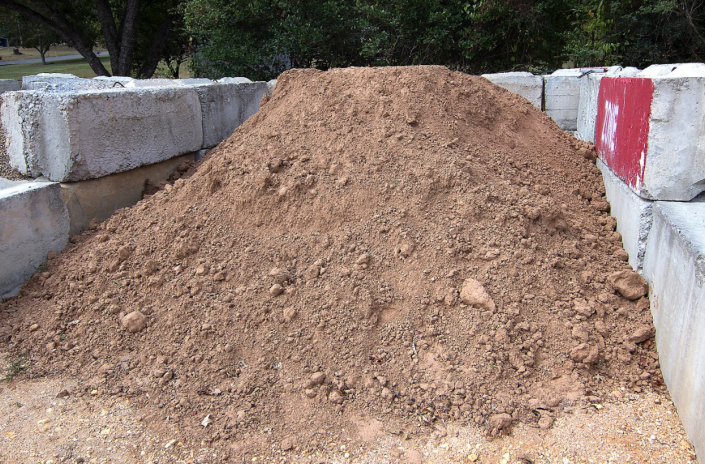 A large dirt pile in a concrete-lined trench with red-and-white barriers on both sides.