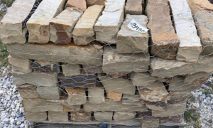 Stacked rough stone blocks with mixed tan, gray, and white surfaces outdoors
