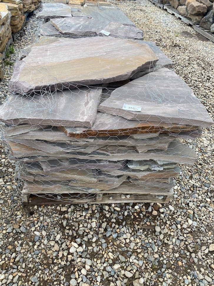 Stack of flat gray stone slabs on gravel outdoors