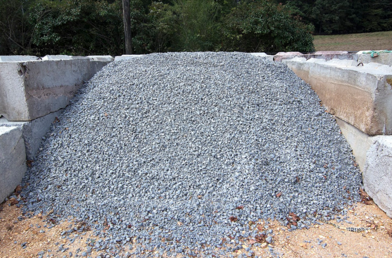 Large pile of gray gravel or crushed stone in a concrete storage bay outdoors