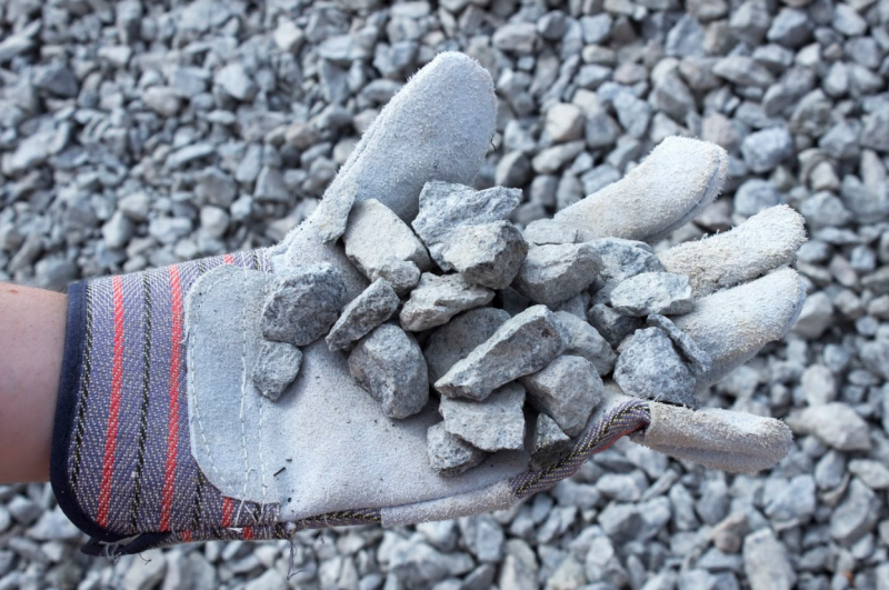 Gloved hand holding small gray rocks over a pile of gravel