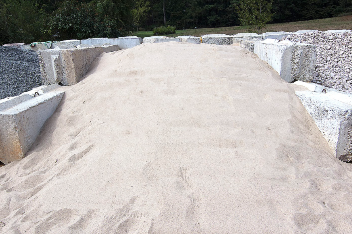 Sandy path bordered by low concrete blocks and gravel in a wooded outdoor area