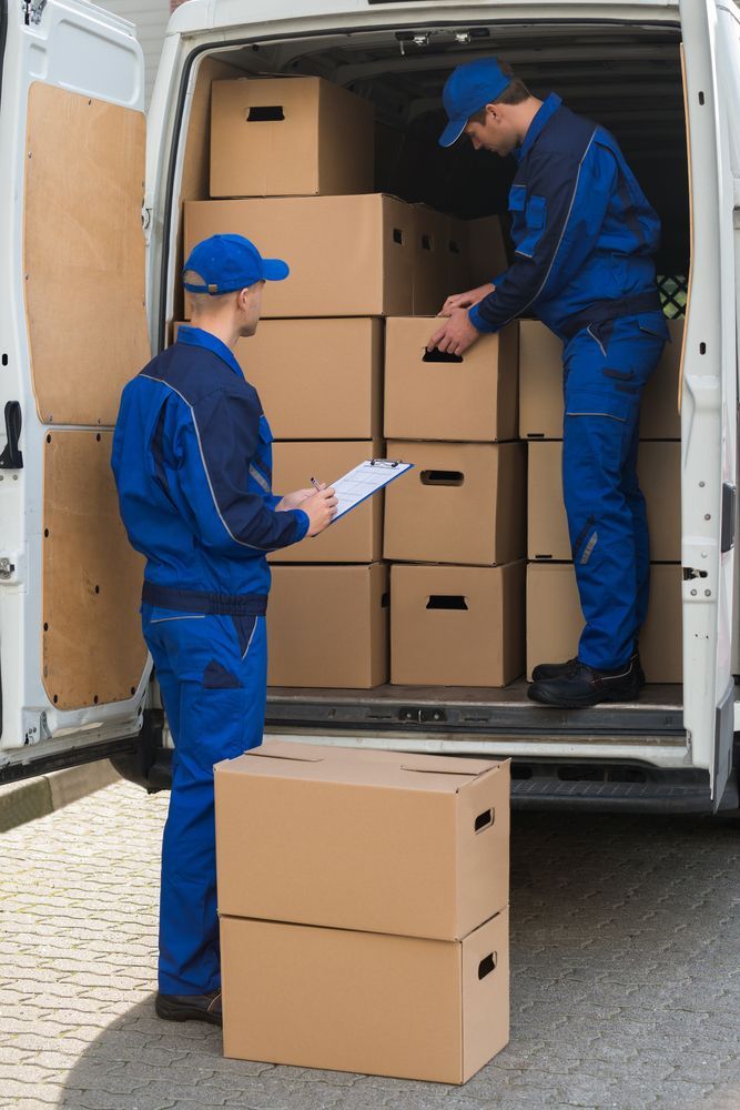 Two Delivery Workers in Blue Uniforms Loading Cardboard Boxes Into a White Van — Access Couriers in Taree, NSW