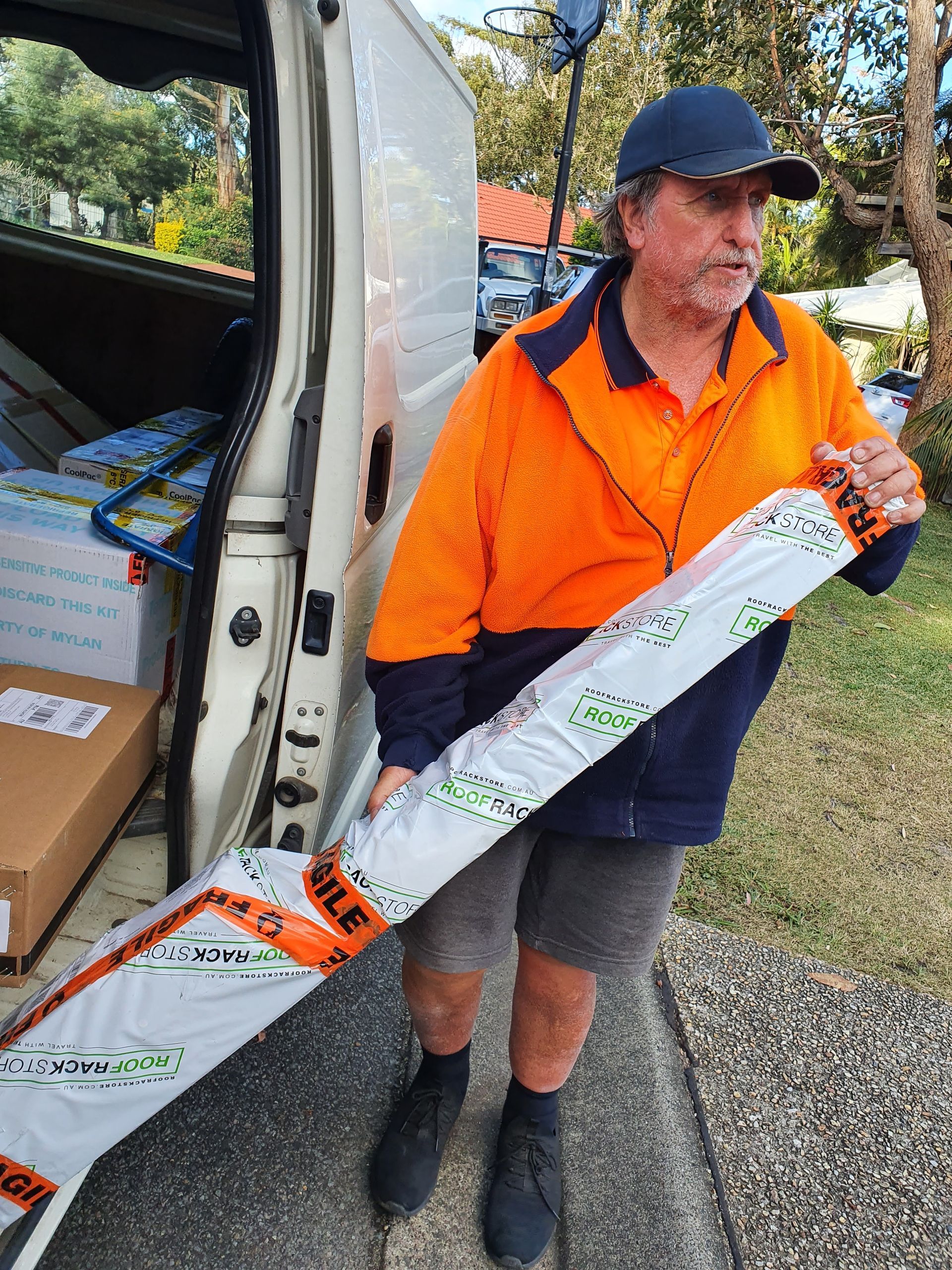 Man In Orange Jacket Unloading a Long Wrapped Item From a Van Outdoors — Access Couriers in Port Macquarie, NSW