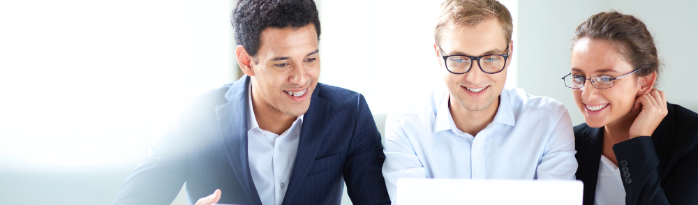 Three business colleagues smile while looking at a laptop.