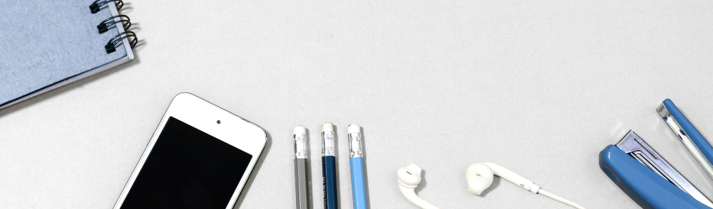 Desk scene with a notebook, phone, pencils, headphones, and stapler.