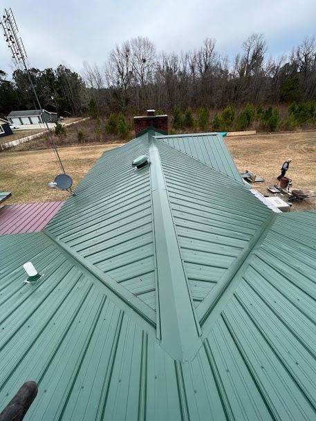 Green metal roof with a chimney in a rural setting.