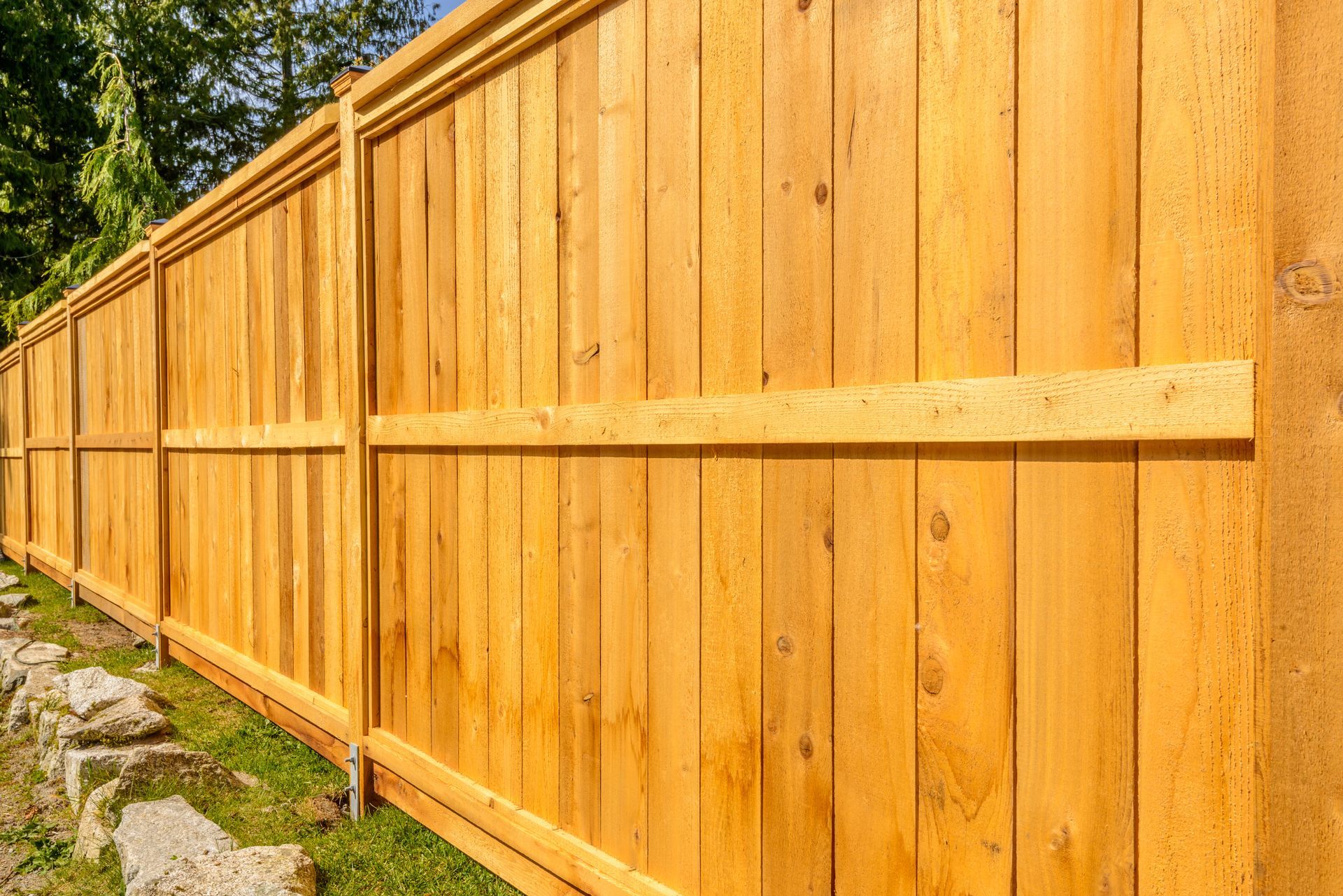 Wood privacy fence with cap rail along a sloped yard.