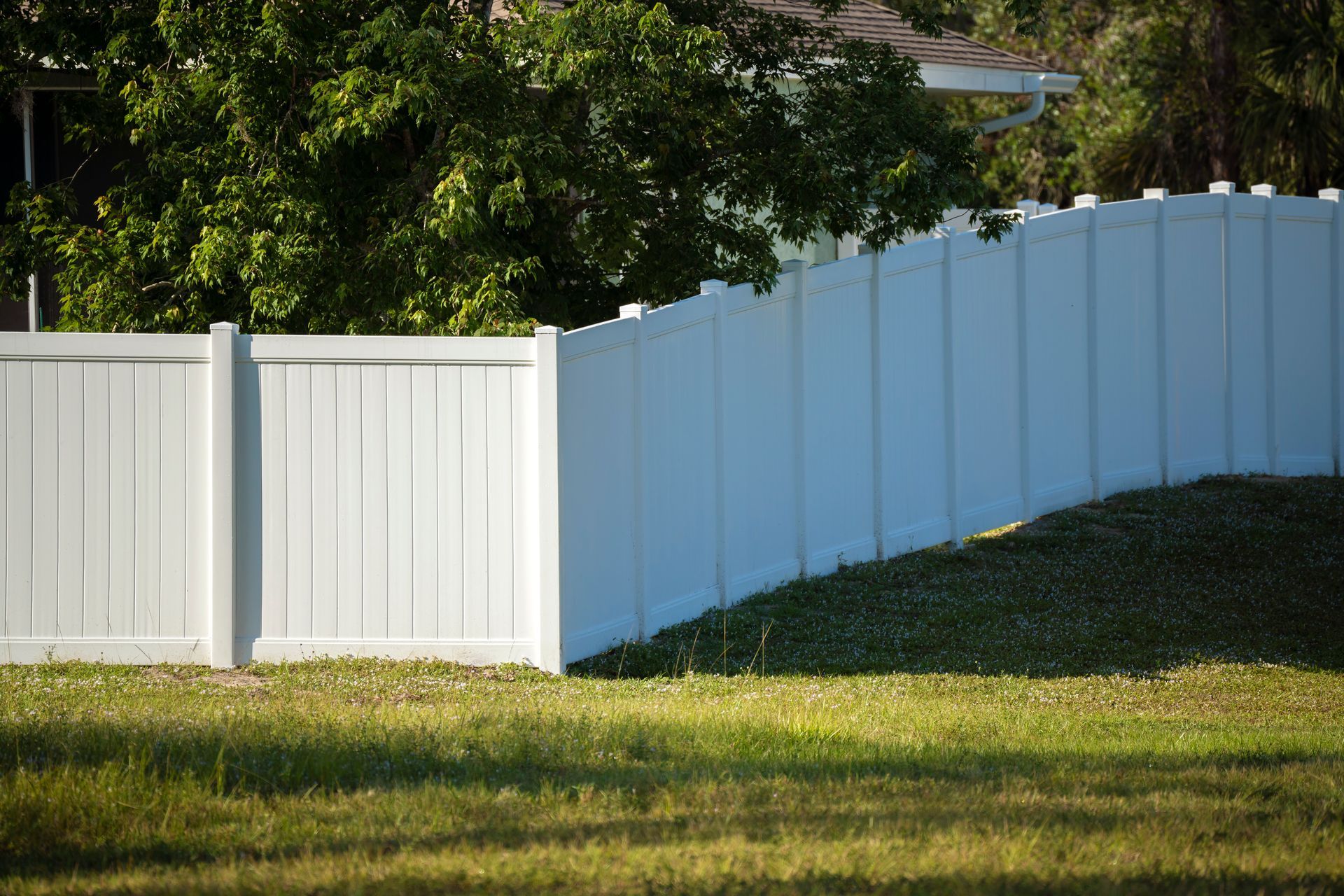 White vinyl privacy fence along a sloped grassy yard.
