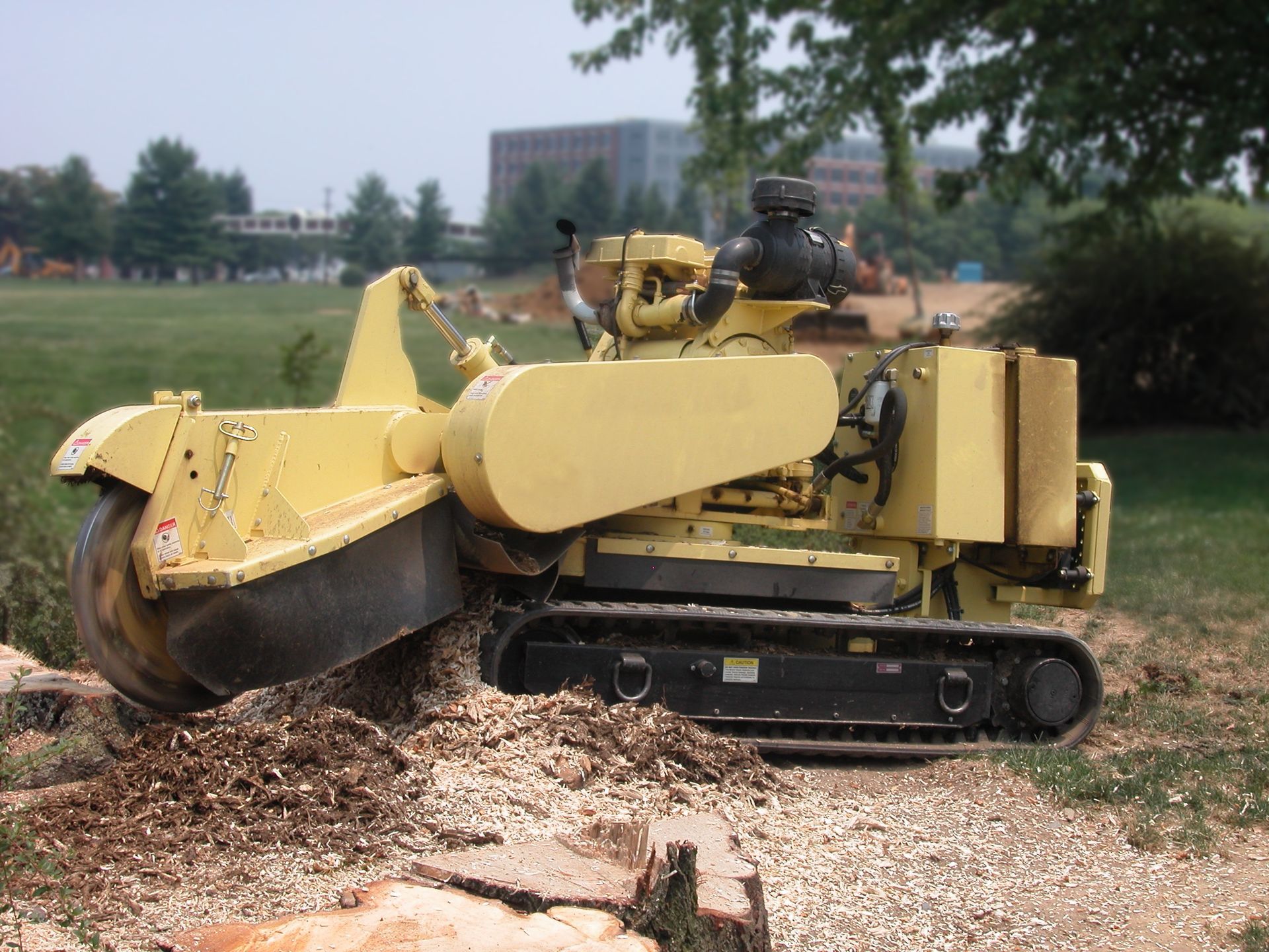 A yellow tractor is cutting a tree stump in a field.