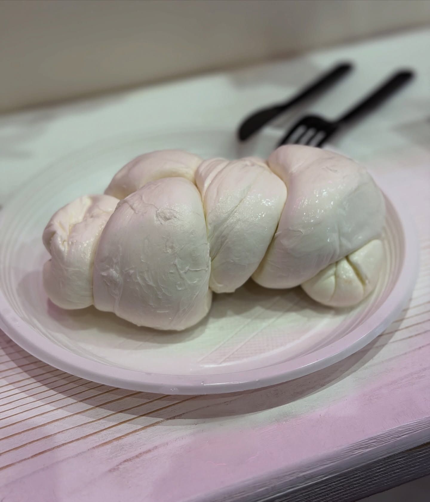 Formaggio bianco annodato su un piatto bianco con forchetta e cucchiaio neri.