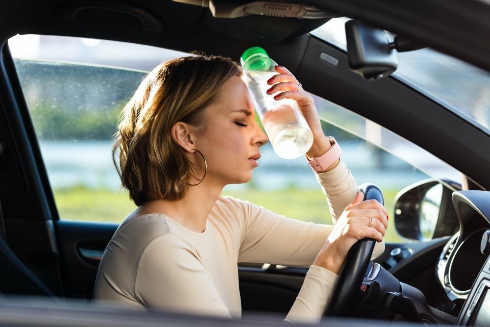 A woman is sitting in a car drinking water from a bottle.