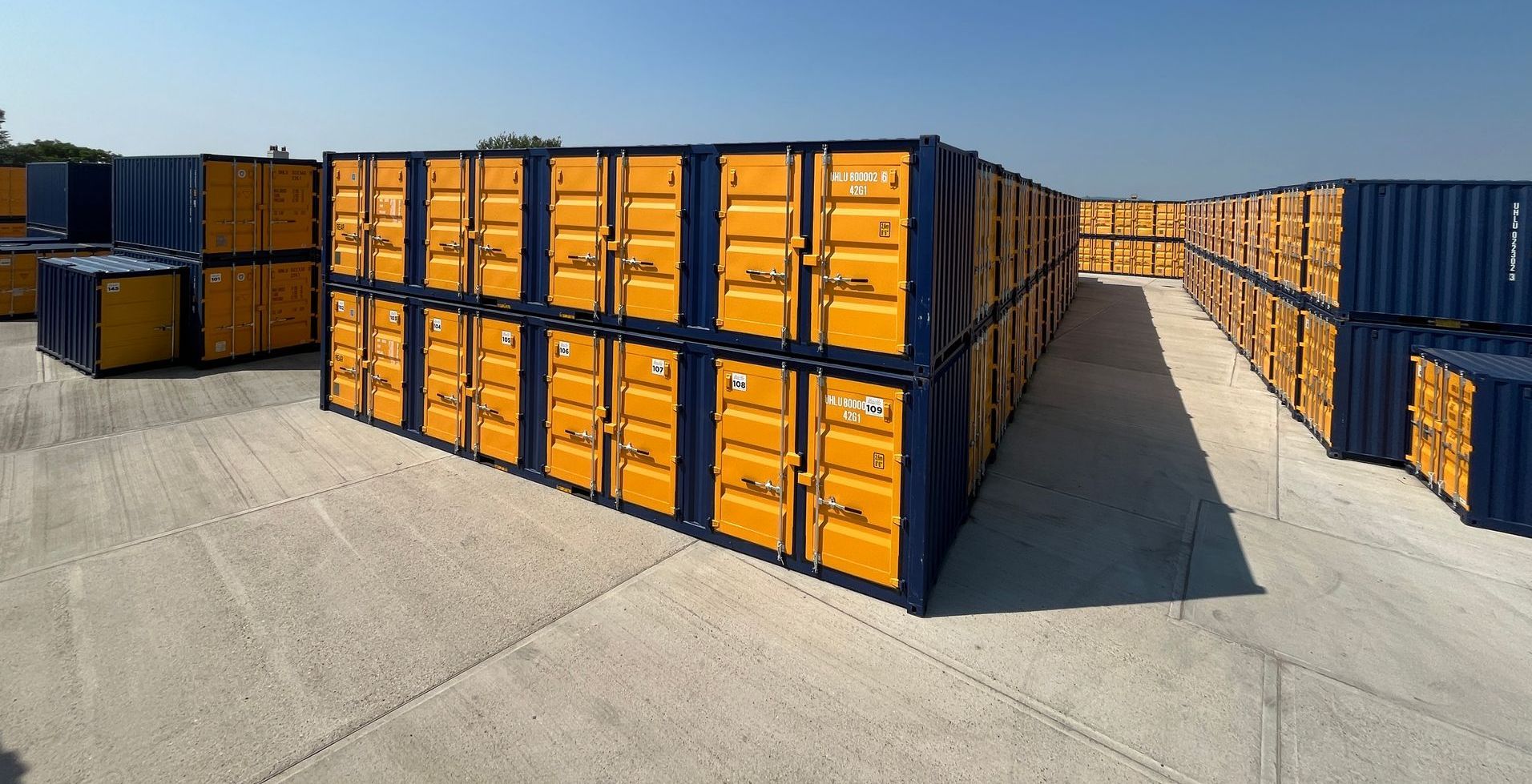 Rows of stacked yellow storage containers with blue frames, on concrete, outdoors.