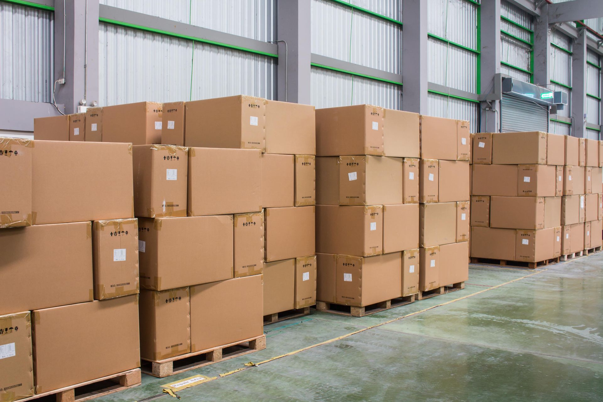 A warehouse filled with lots of cardboard boxes on wooden pallets.