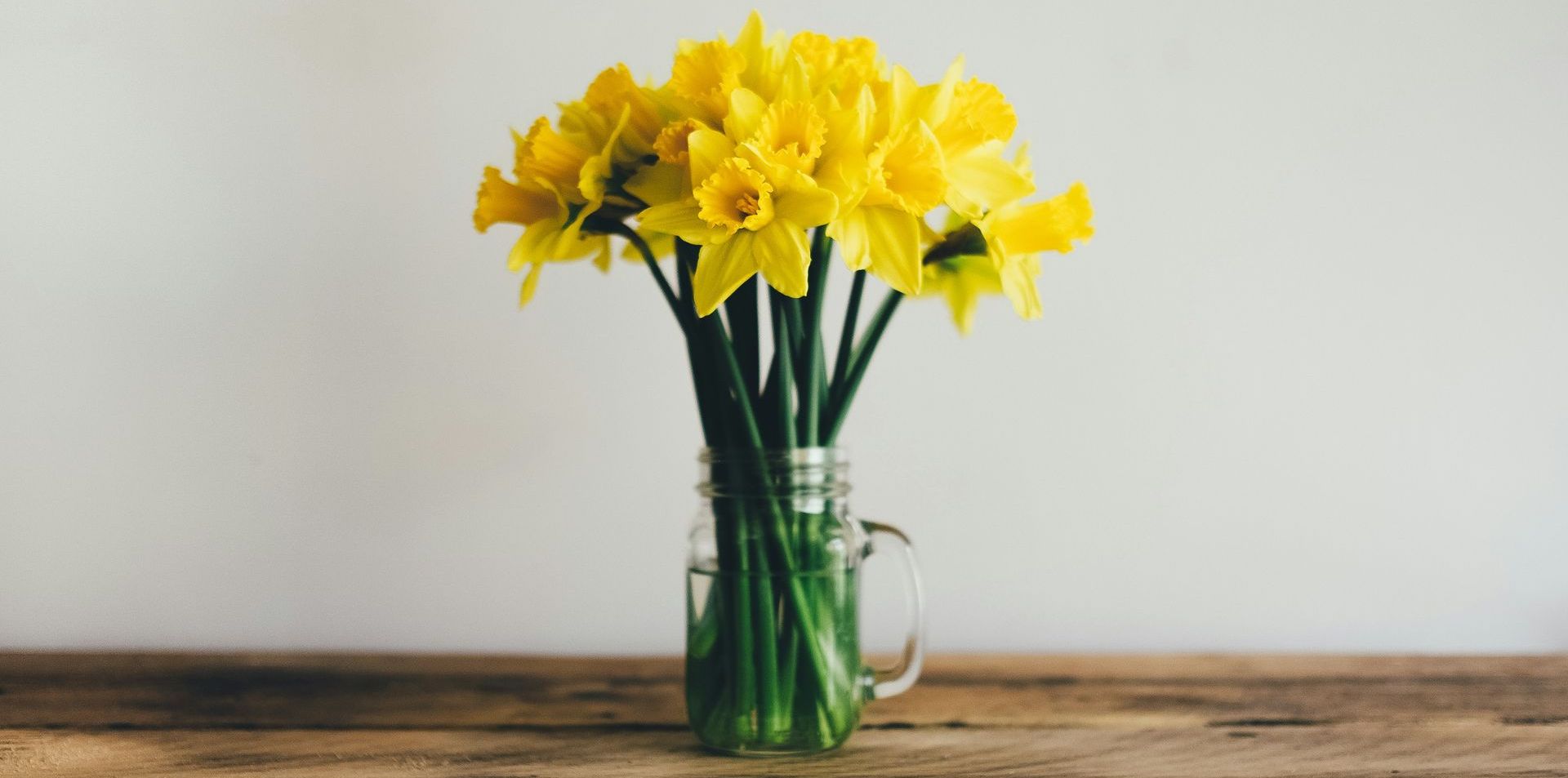 A vase filled with yellow flowers is sitting on a wooden table.