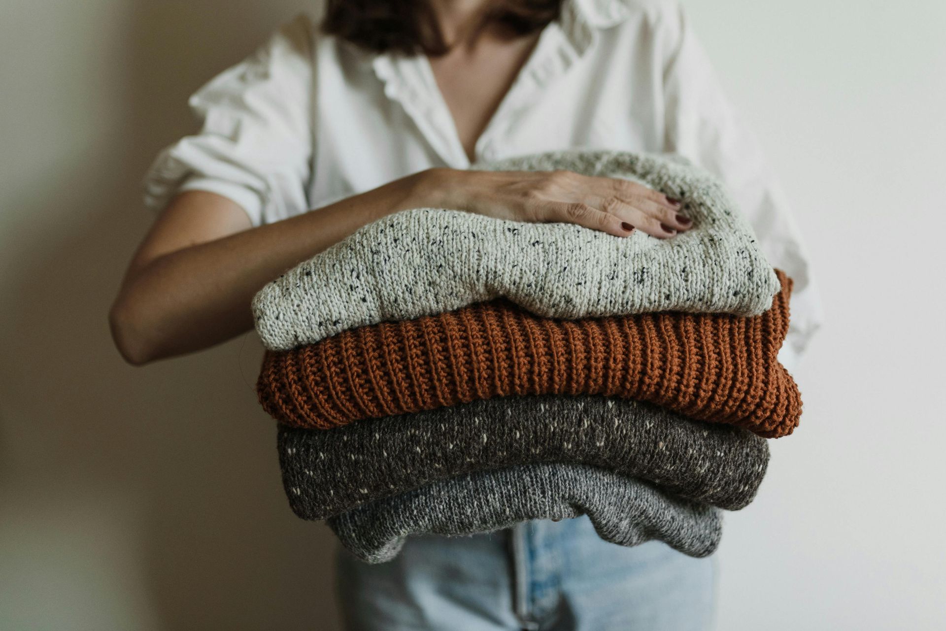 lady holding four folded jumpers