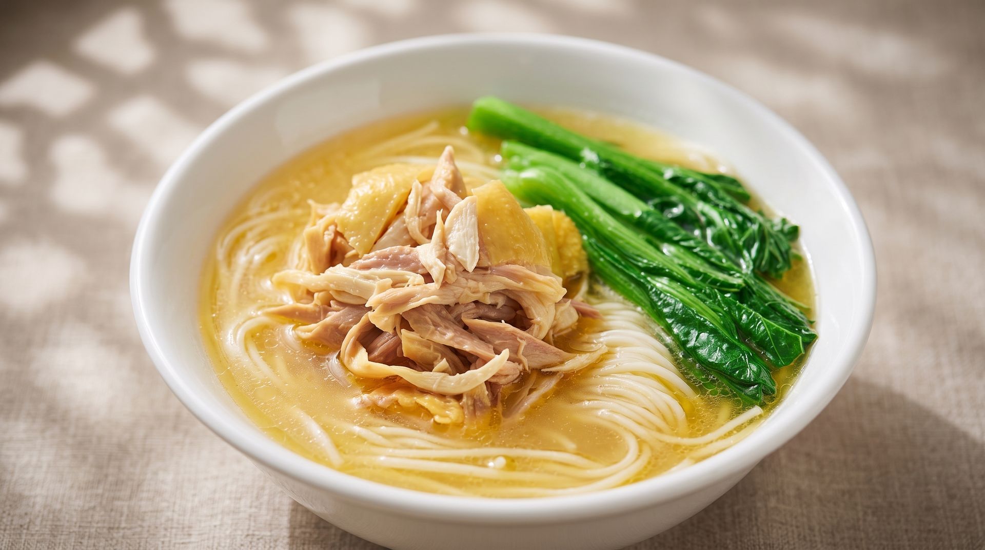 Bowl of noodle soup with sliced meat and green vegetables in a light broth