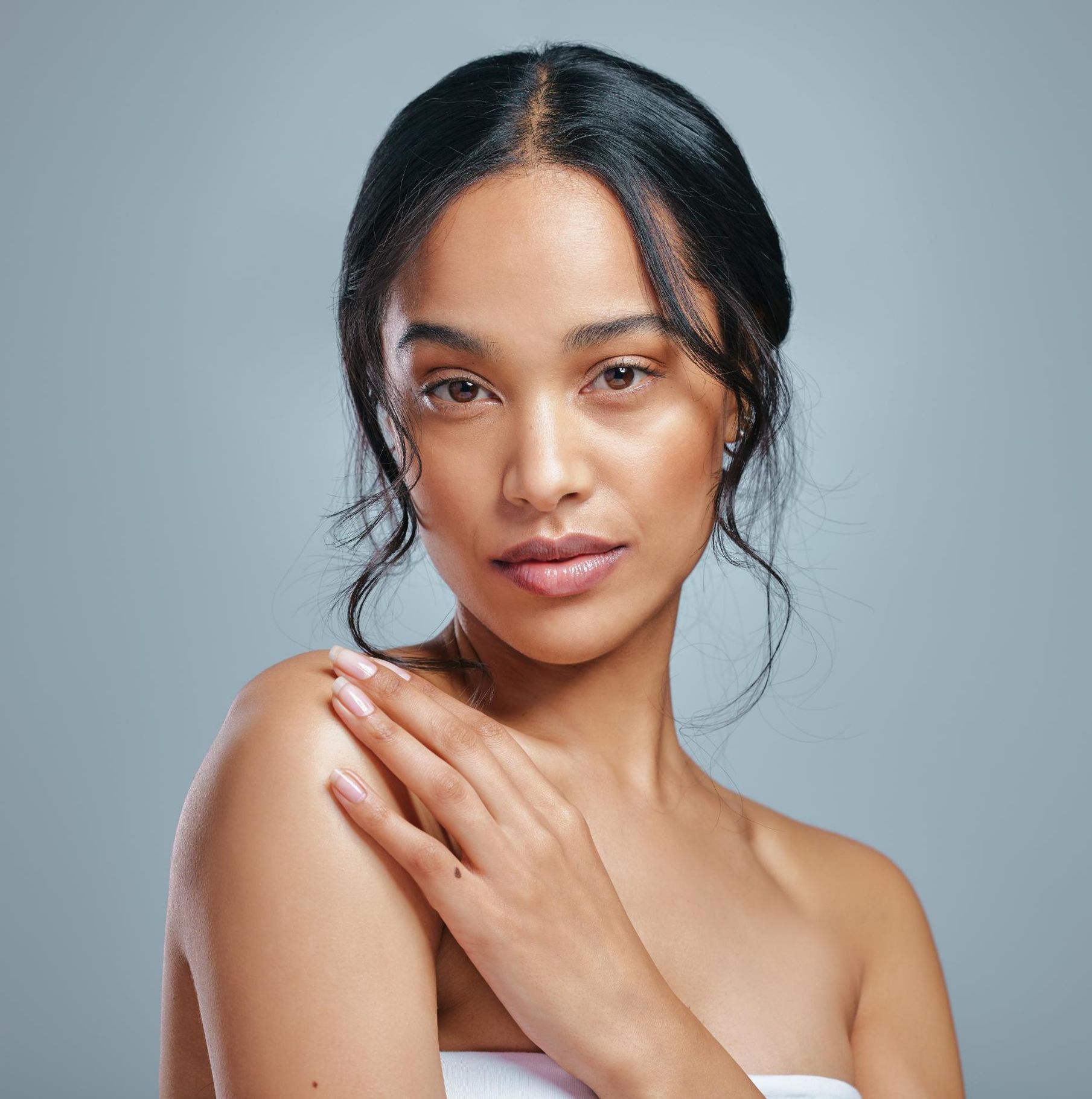A woman with a hand on her shoulder is looking at the camera.