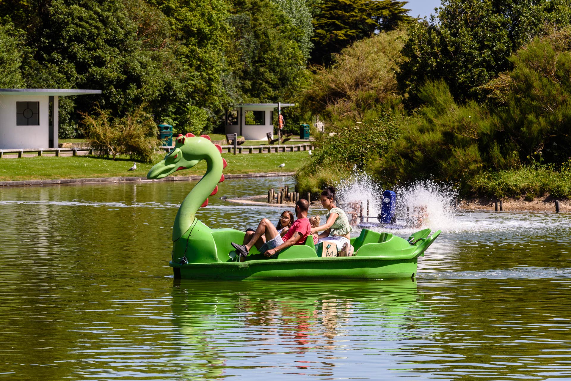 A  family enjoying  a bright green dragon boat style pedalo on Mewsbrook Boating Lake , Littlehampton.