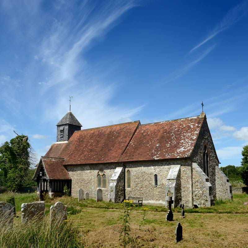 An historic Sussex village church with churchyard, wildflowers and trees in the height of summer.