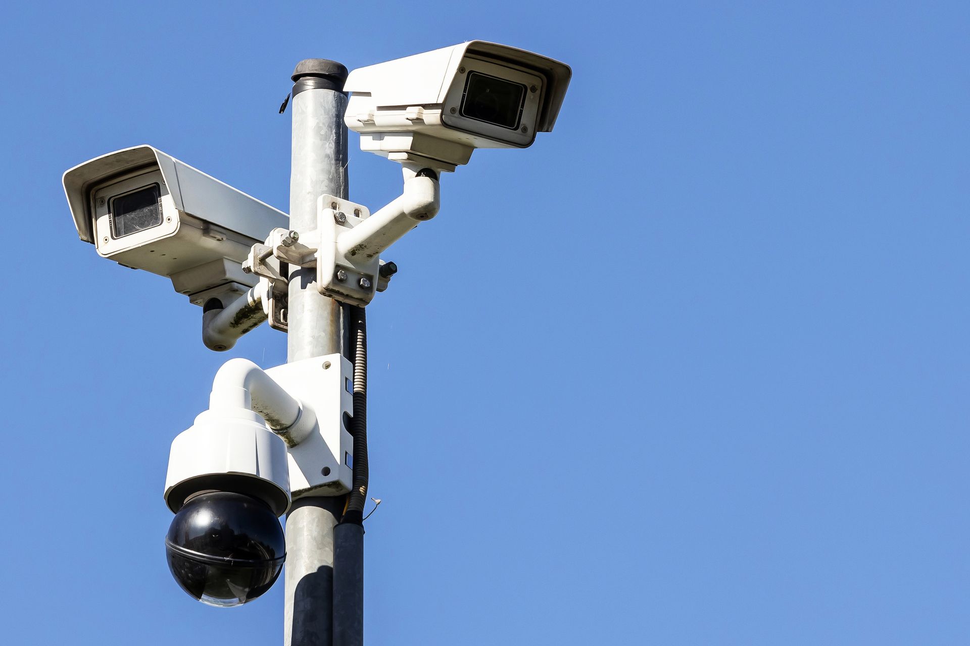 Surveillance cameras mounted on a pole against a clear blue sky.