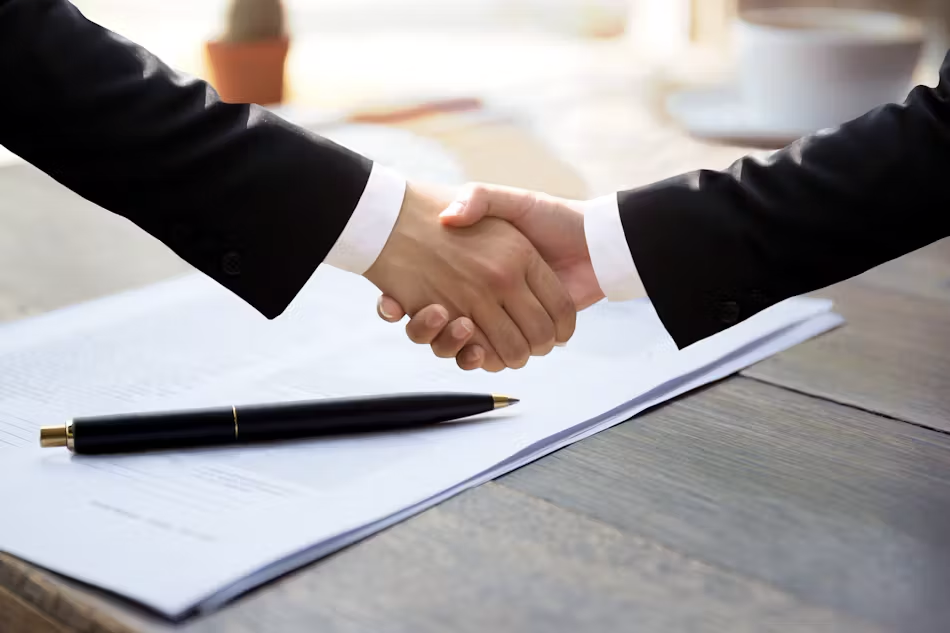 Two business people are shaking hands over a signed contract.