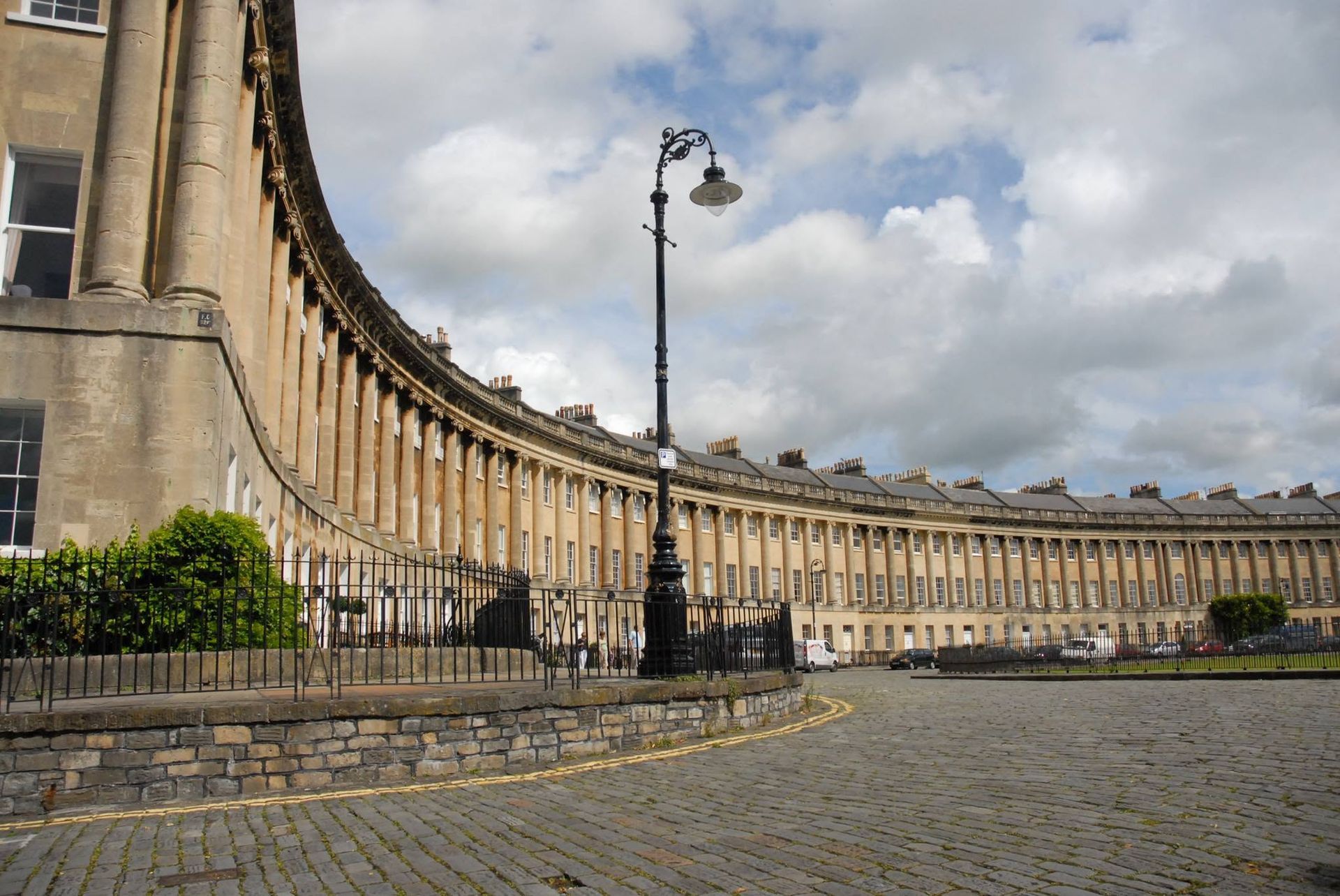 Curved historic stone terrace with black lampposts and cobblestone street under a cloudy sky