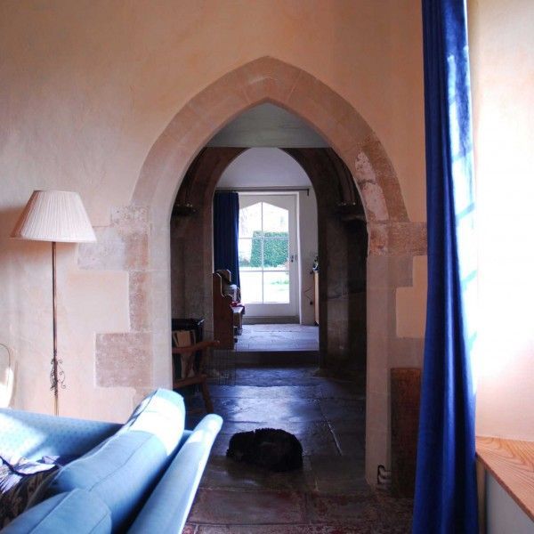 Living room view through a stone archway to a bright doorway, with blue sofa, lamp, and curtains
