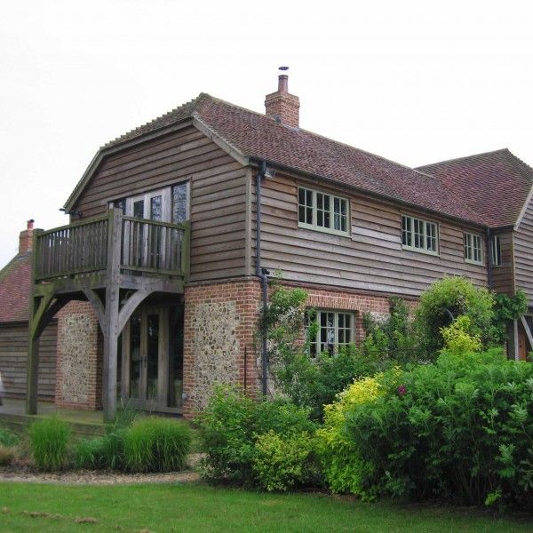 Two-story brick and wood house with balcony and garden shrubs