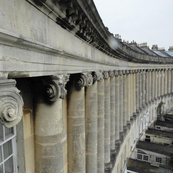 Curved colonnade of stone columns supporting a classical building facade in soft light
