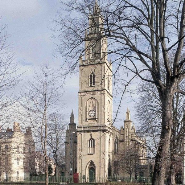 Stone church tower with a clock, framed by bare trees under a pale sky.