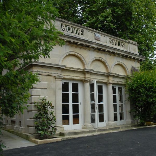 Small stone building with arched windows and a sign above the entrance, surrounded by trees