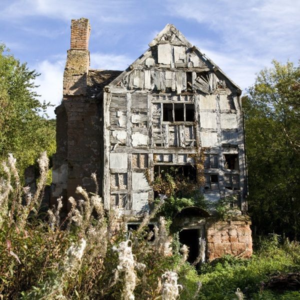Abandoned, weathered stone house with broken windows and overgrown vegetation in front