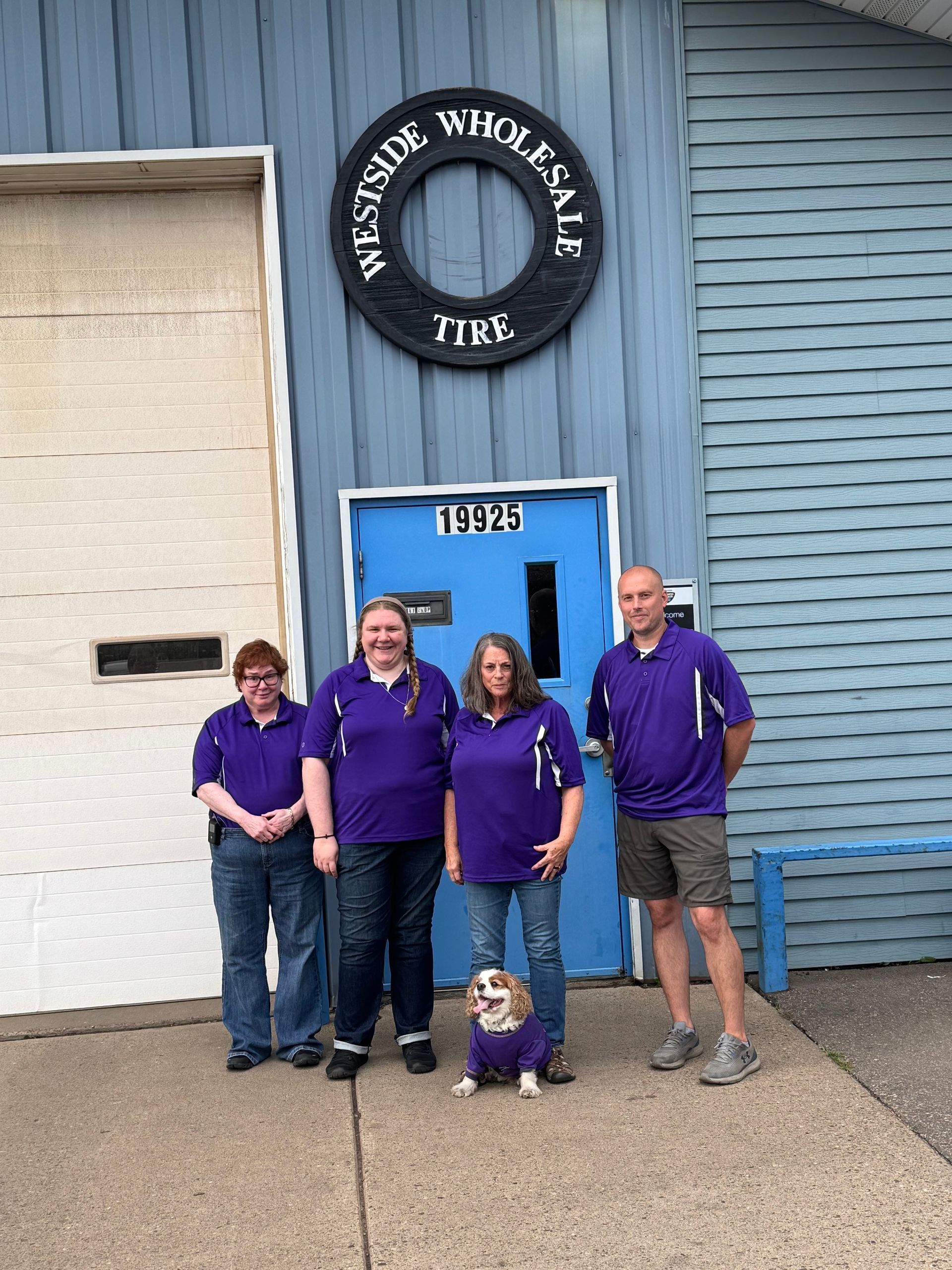 Four people in purple shirts stand outside a blue building with a circular sign and door marked 1175.