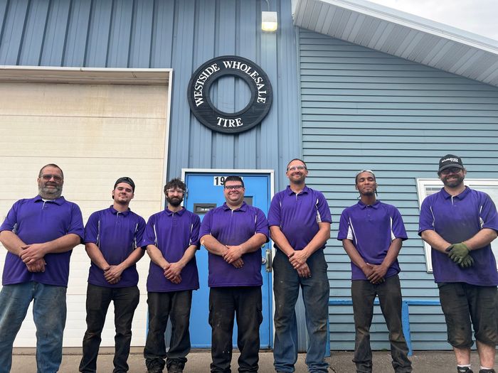 Group of people in purple shirts standing outside a blue building with a circular sign.