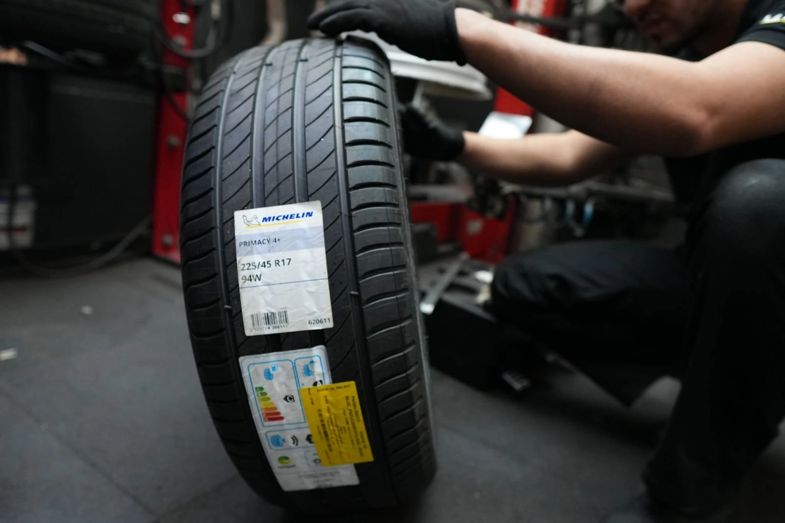 Oficina mecânica com carros em elevadores, mecânicos trabalhando e exposição de pneus Bridgestone.