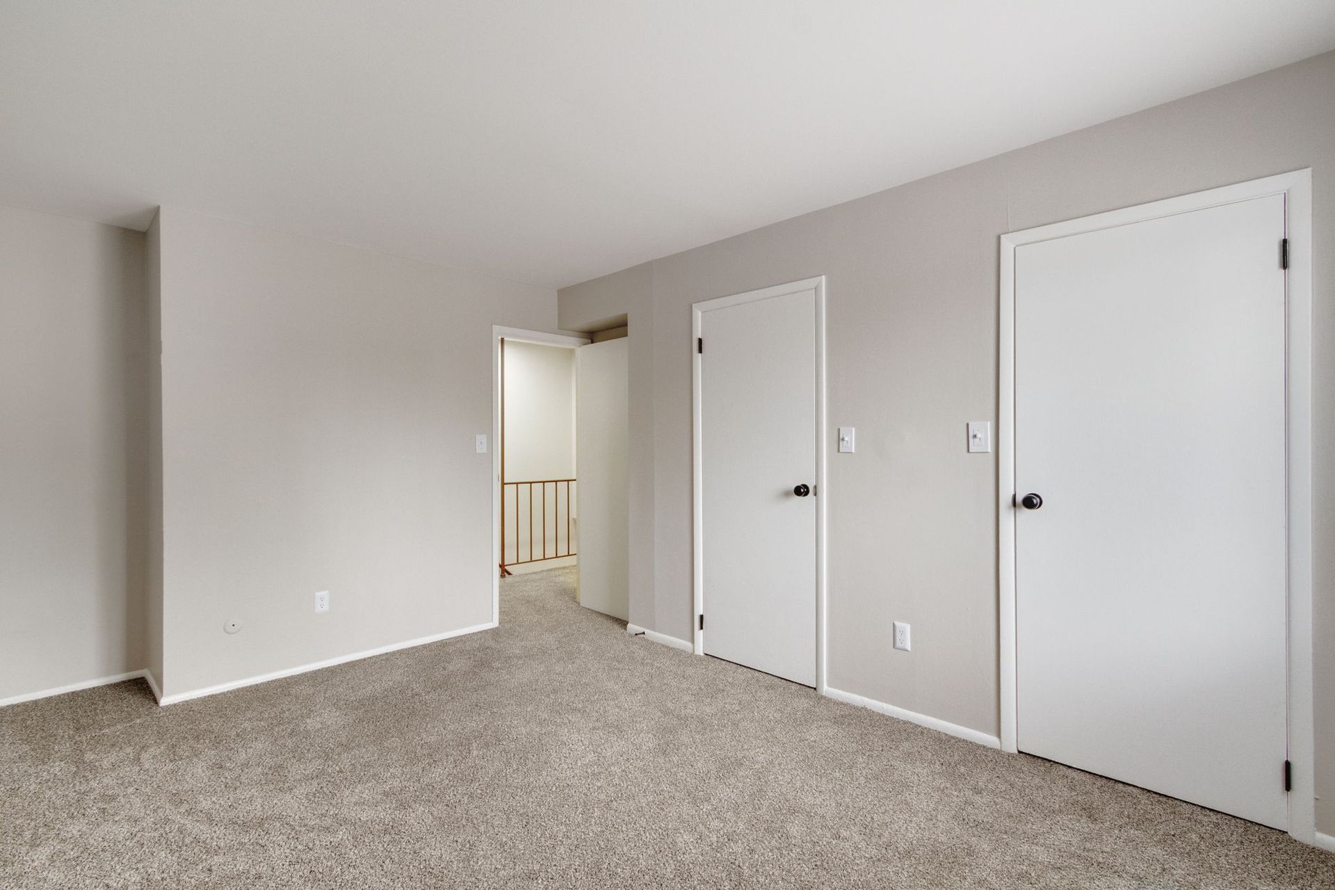 Empty bedroom with gray carpet, light gray walls, two white closets, and open doorway.