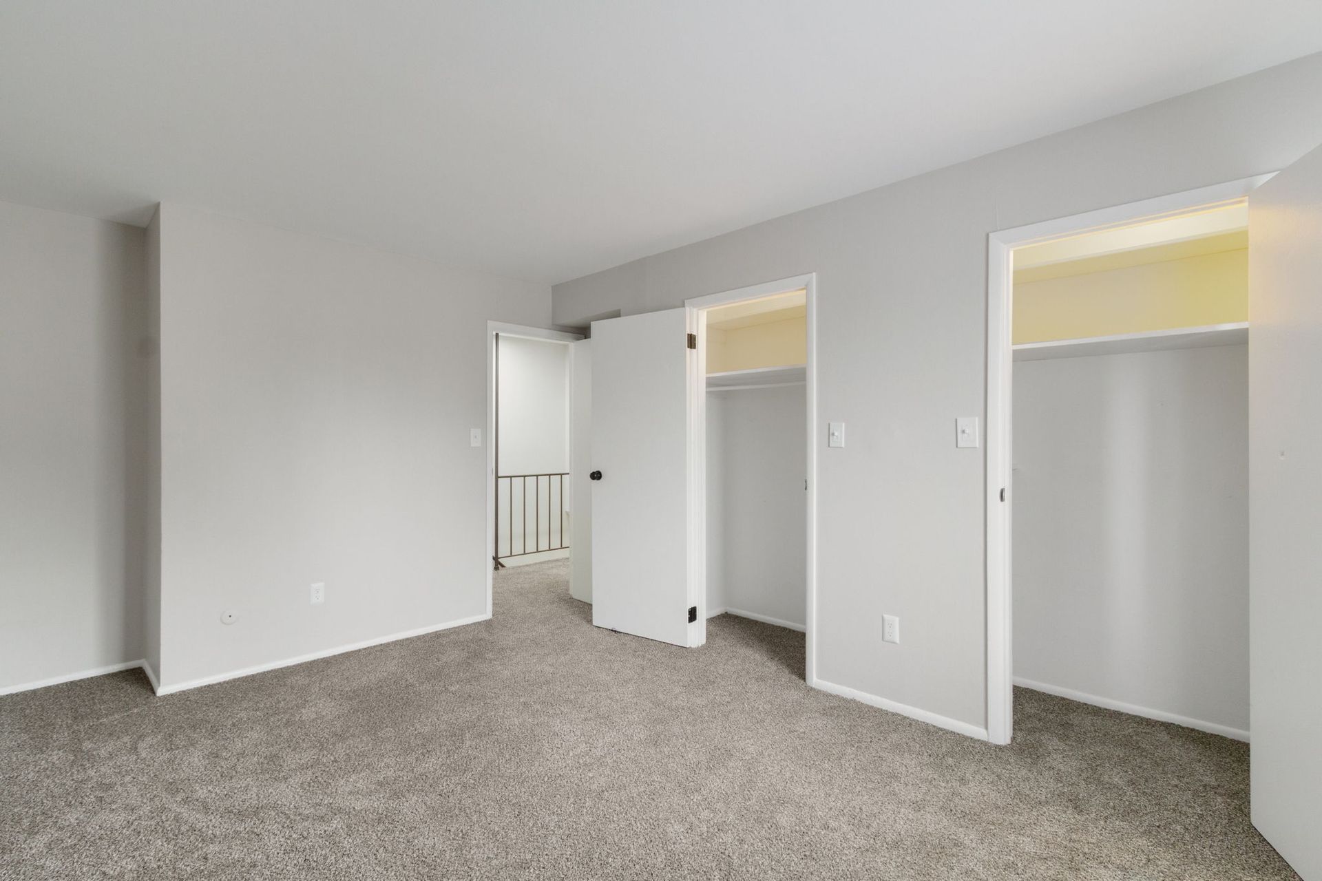 Empty bedroom with gray carpet, three white doors, and stairs in the background.
