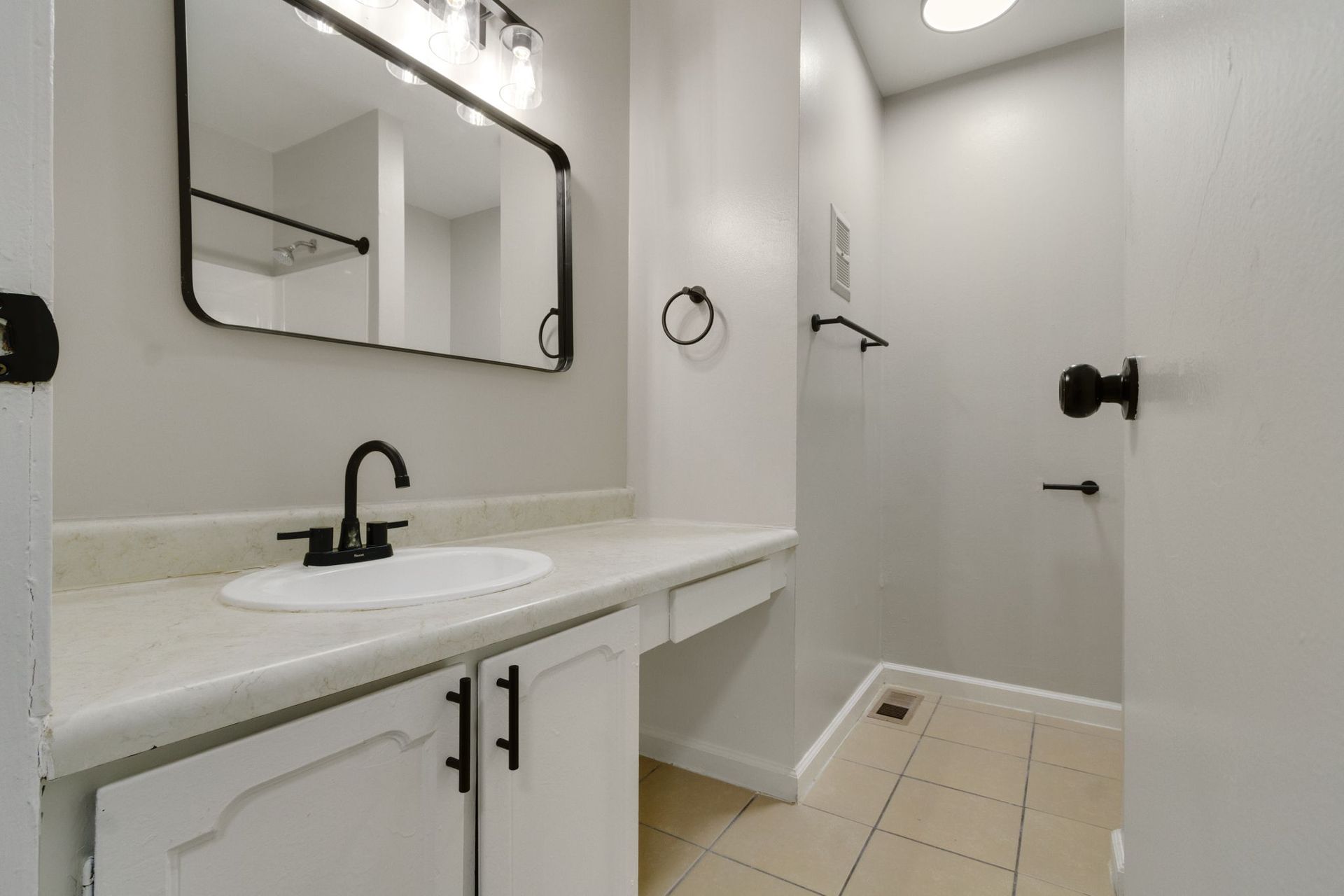 Bathroom with white cabinets, gray walls, black fixtures, and beige tile floor.