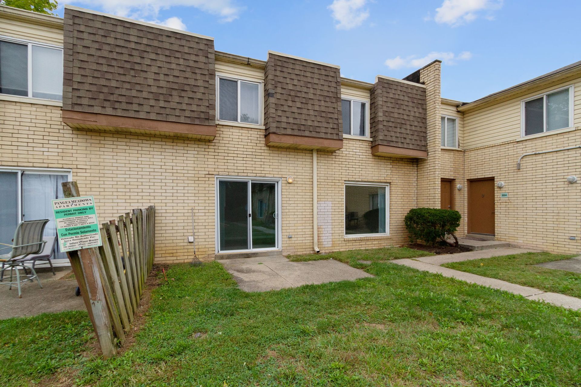 Rear view of a brick townhouse with a small yard, brown roof features, and a wooden fence.