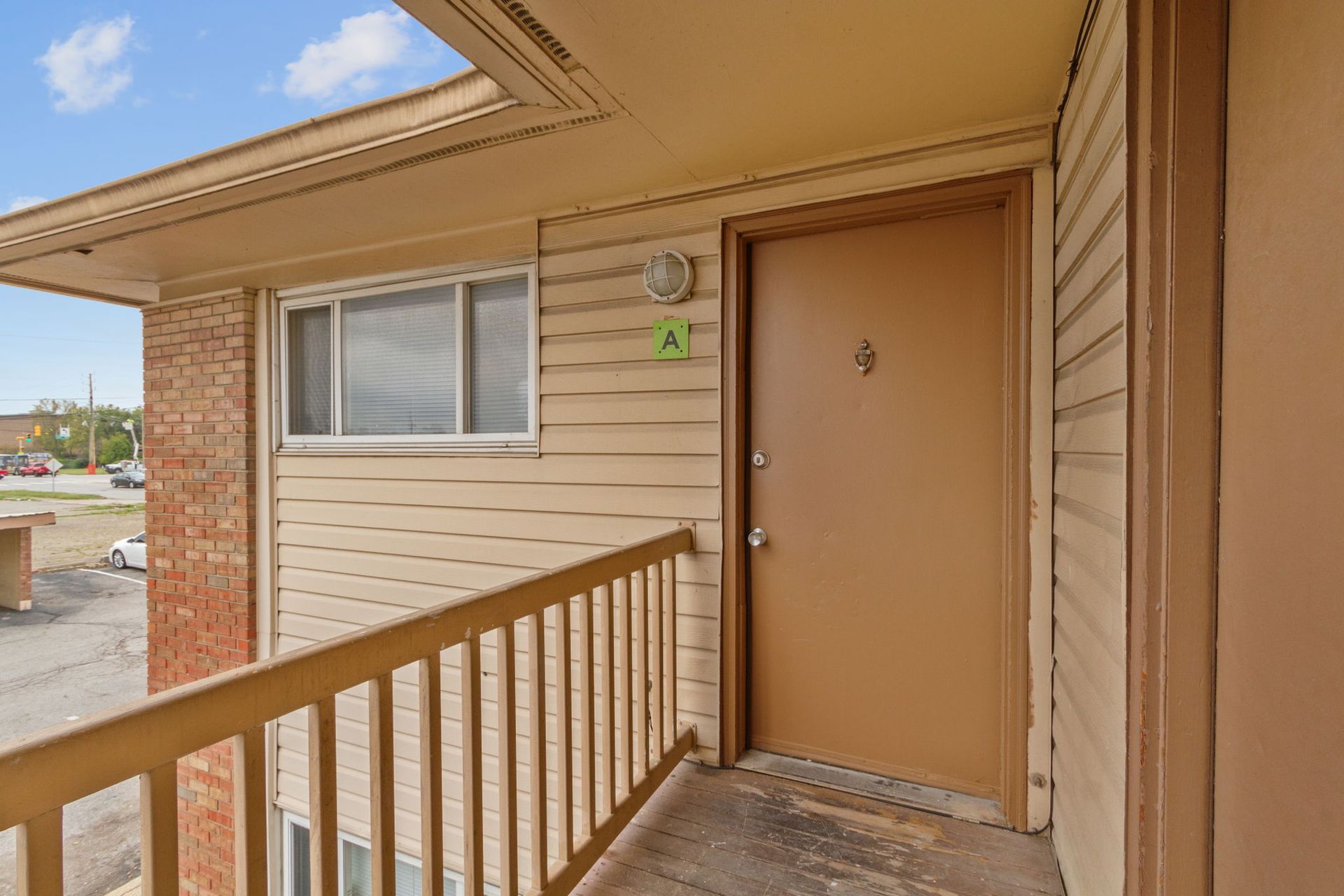 Exterior apartment doorway with tan door, window, and brown railing.