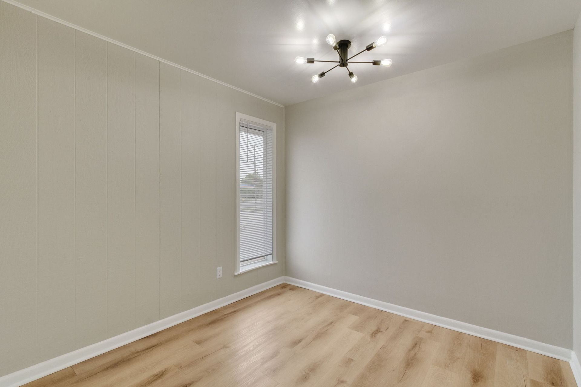 Empty room with light wood-look floor, light gray walls, small window, and a starburst ceiling light.