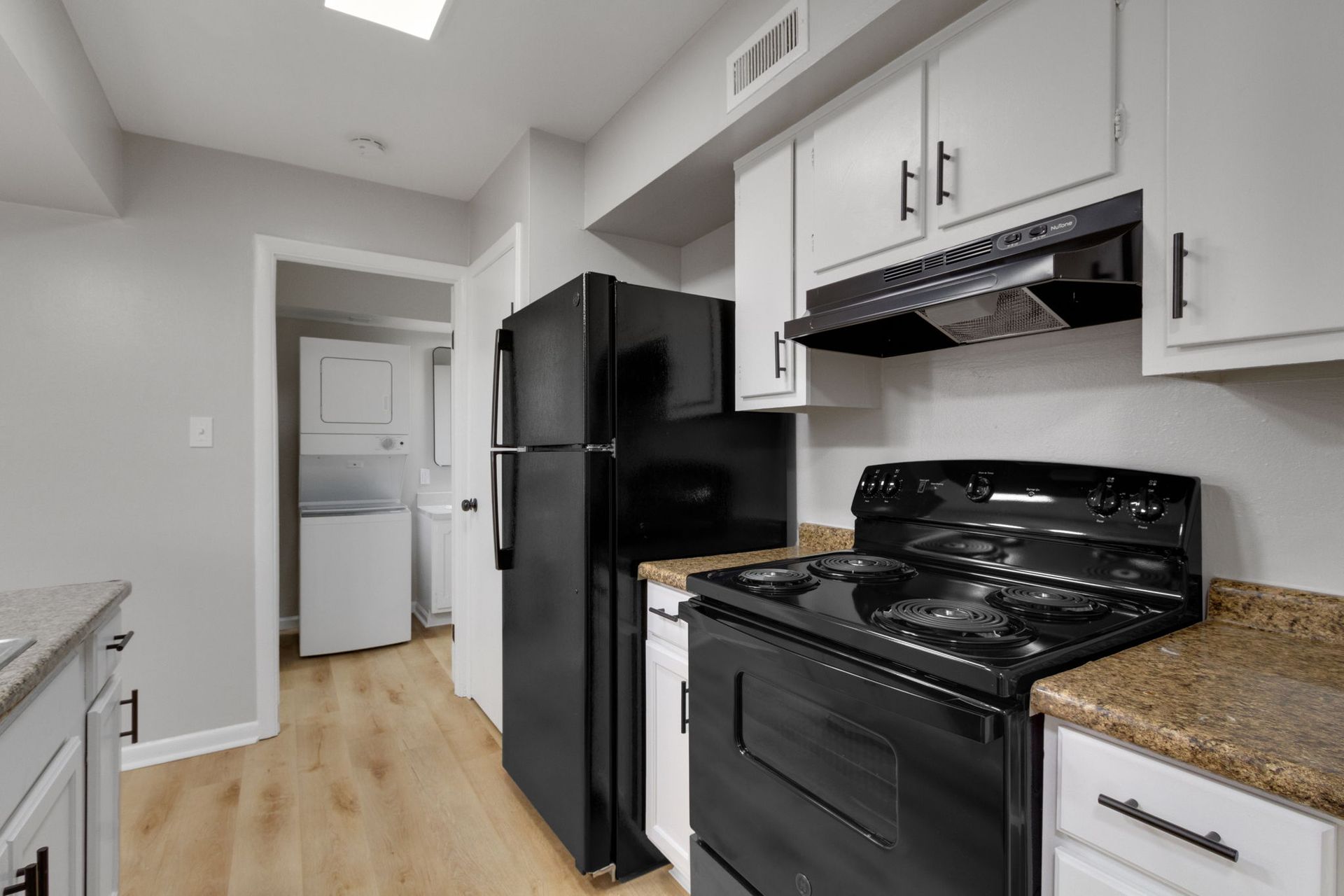 Kitchen with white cabinets, black appliances, and light wood-look flooring.