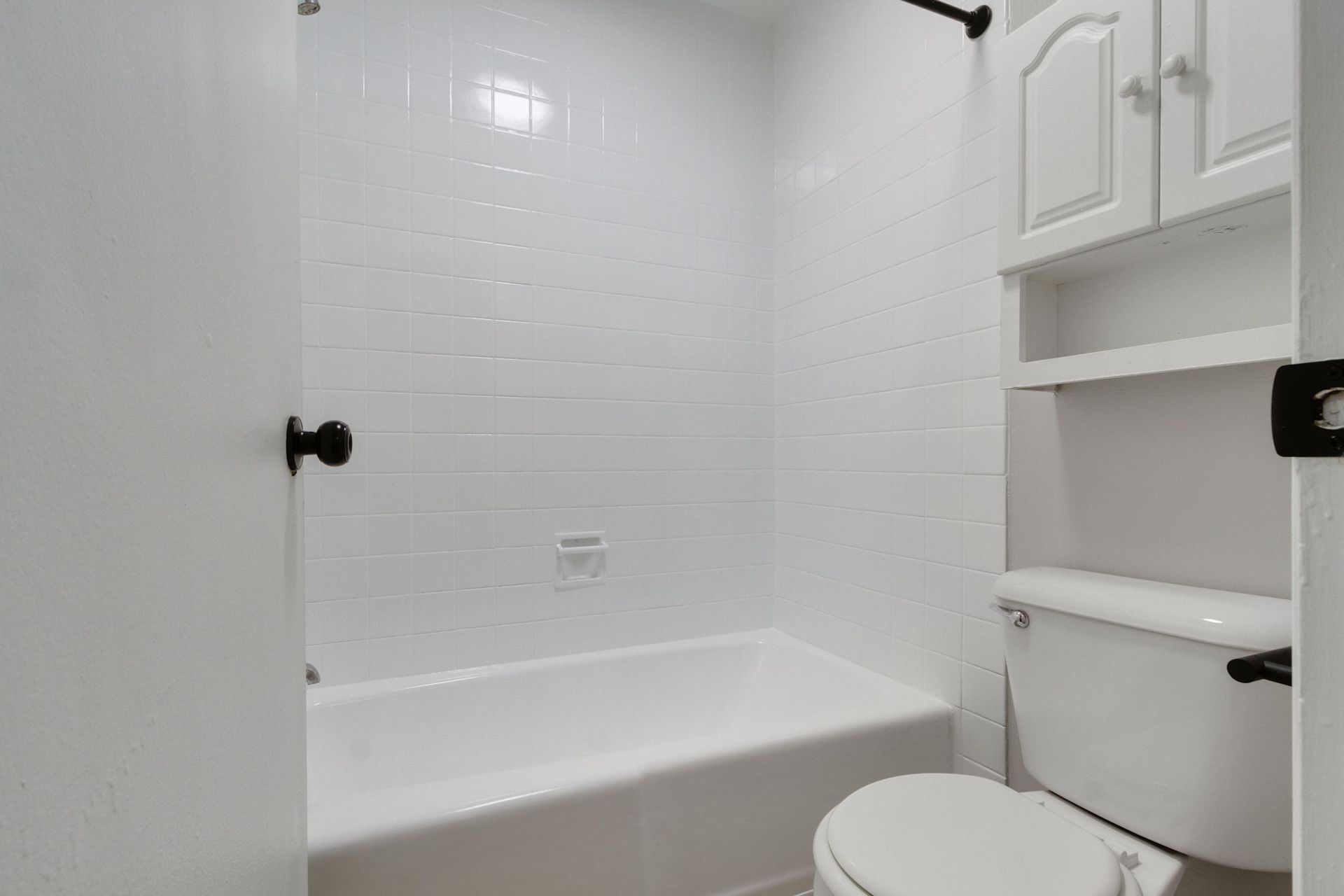 White bathroom with a bathtub, toilet, and storage cabinet.