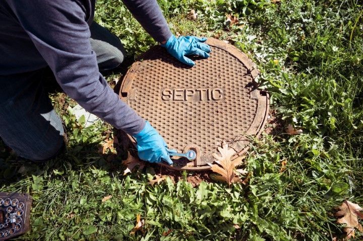 Person in blue gloves lifting a round manhole cover in grass