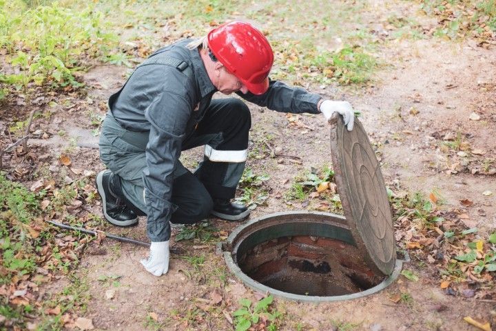 Worker in red hard hat opening a manhole cover outdoors