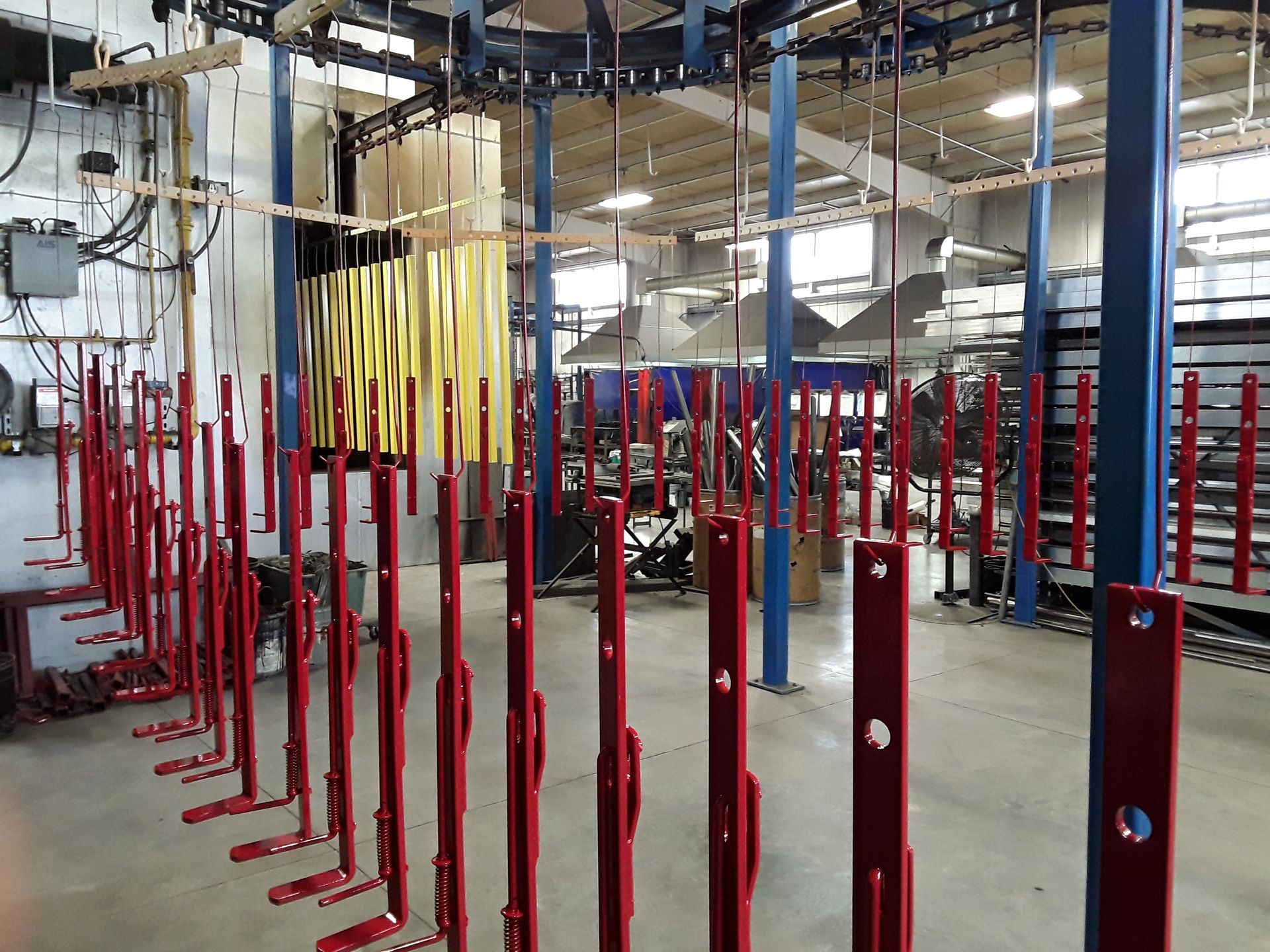 Red painted metal parts hanging from an overhead conveyor system in a factory.