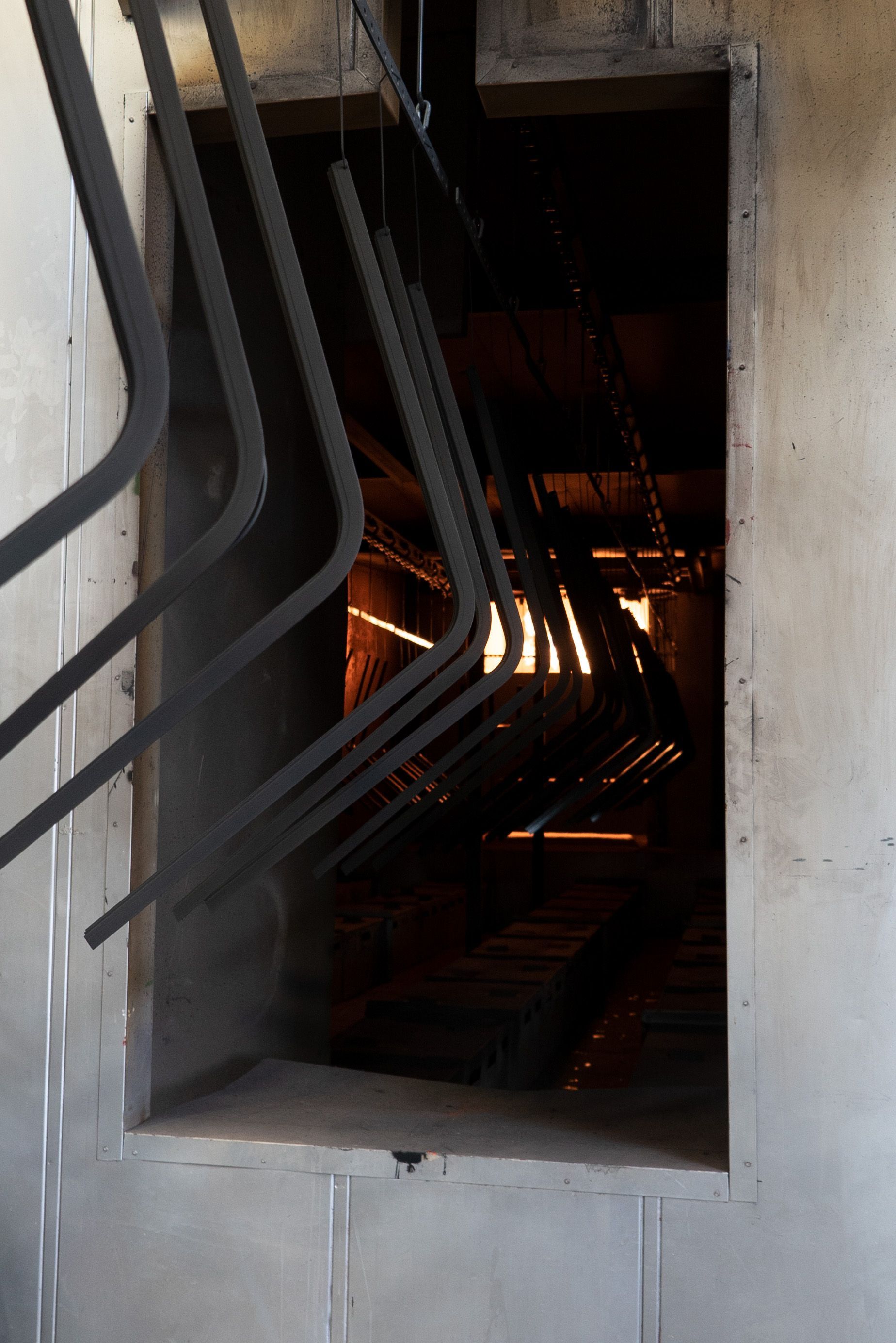 Dark metal parts hanging inside an industrial oven, illuminated by a warm glow.