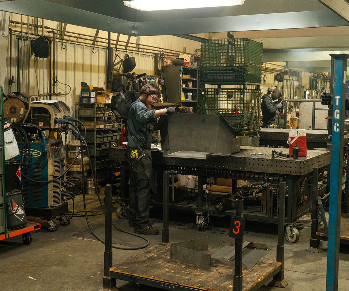 A person welding metal in a workshop. Sparks fly. Various tools and equipment are present.