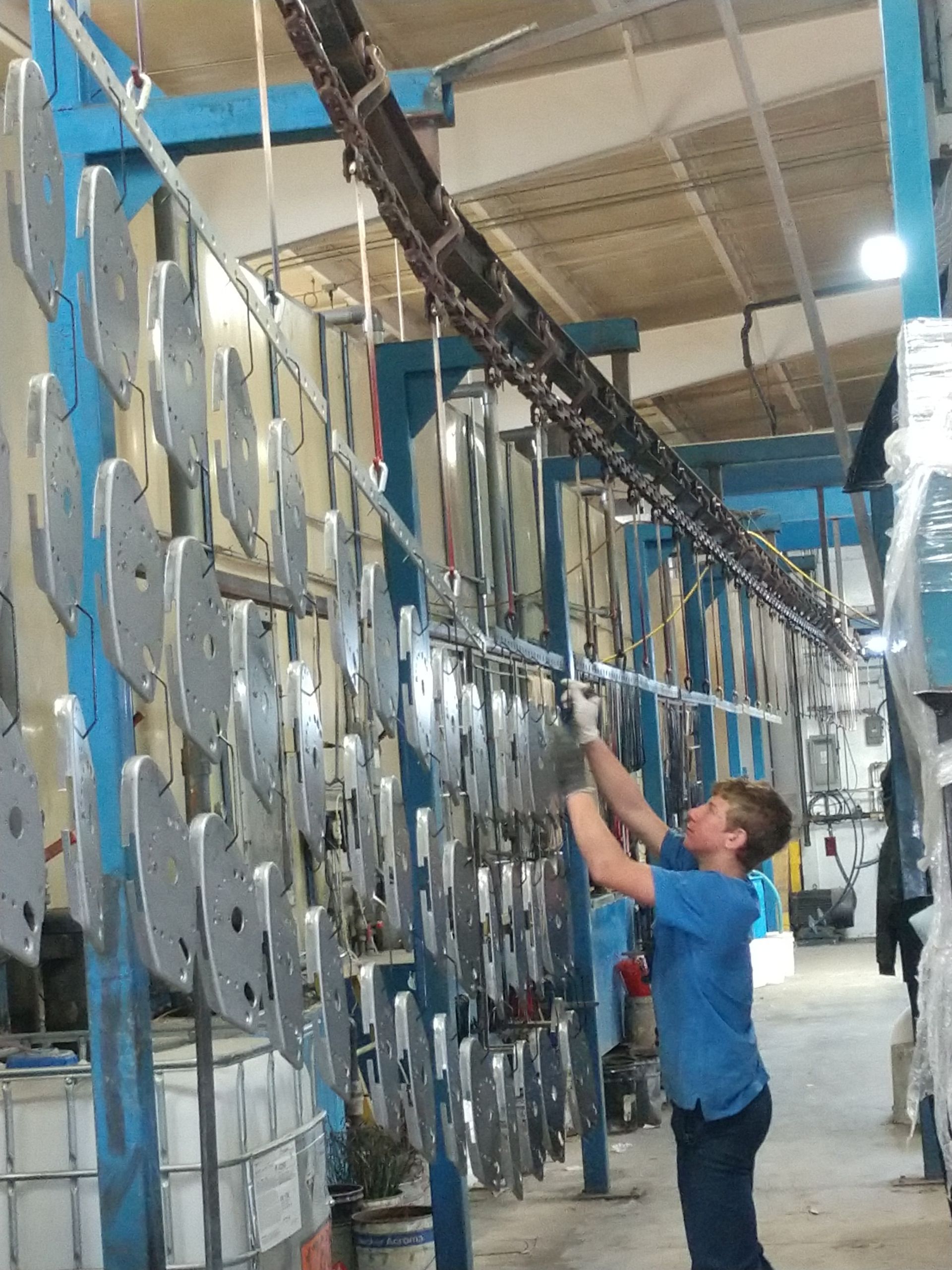 Person in blue shirt hanging metal objects on a conveyor in a factory.